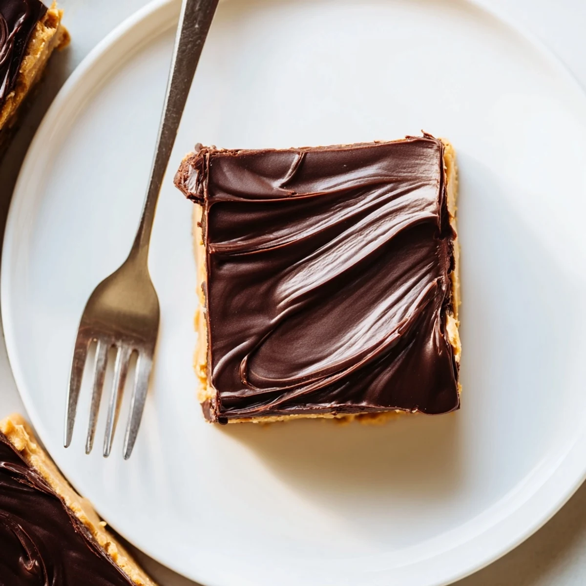 Golden peanut butter bars with glossy chocolate topping cut into neat squares on a white serving plate