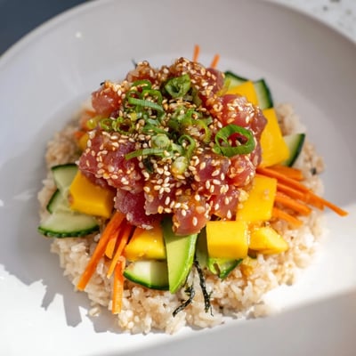 Spicy Tuna Poke Bowl with Mango features marinated tuna, crisp veggies, and sesame seeds, served with lime for a bright finish.  