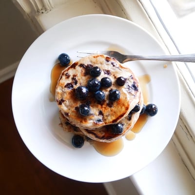 Steam rising from warm protein banana pancakes served on a white plate with scattered berries