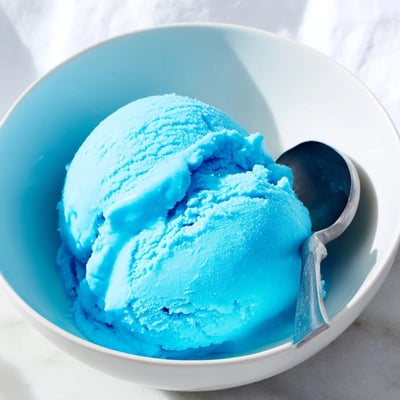 Vibrant blue homemade Blue Moon ice cream served in a bowl topped with whipped cream